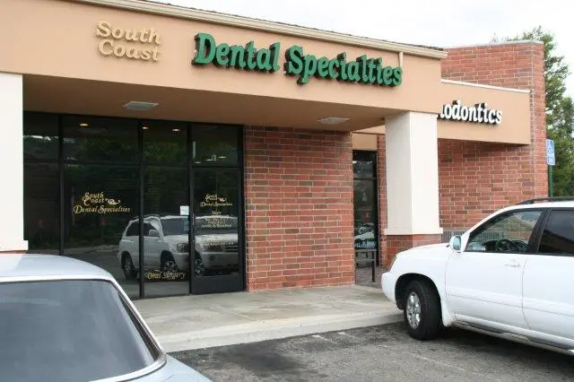 “Dental Specialties” office exterior: brick facade, glass entrance, green signage; white SUV and silver car parked in lot