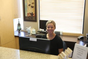 A woman is standing behind a reception desk in what appears to be an office or medical setting. 