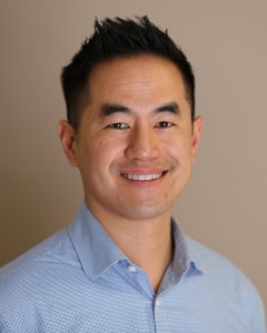 A man with short, neatly styled black hair is smiling warmly.